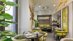 Een moderne eetruimte met ronde tafels en gele stoelen met kussens, omringd door grote groene planten.