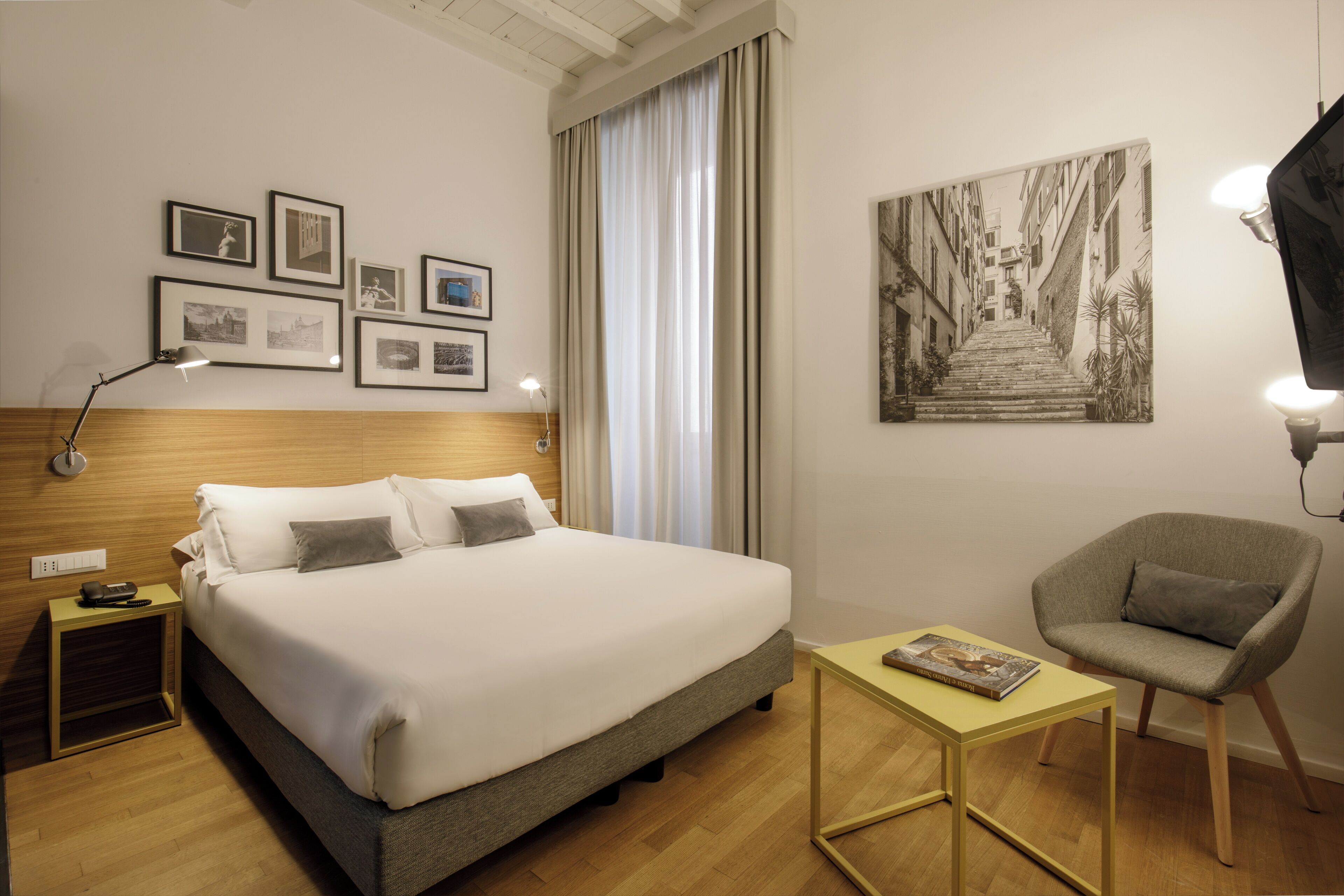A hotel room with a large bed, a bedside table with a lamp, a chair, and framed pictures on the wall.