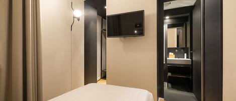 A bedroom with a bed, a flat-screen TV mounted on the wall, and a mirror in the adjacent room.
