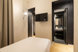 A bedroom with a bed, a flat-screen TV mounted on the wall, and a mirror in the adjacent room.