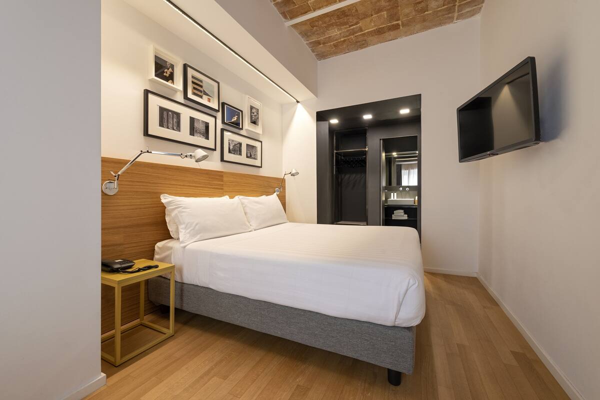 Un dormitorio moderno con cama, mesita de noche, lámpara, cuadros enmarcados y televisor.