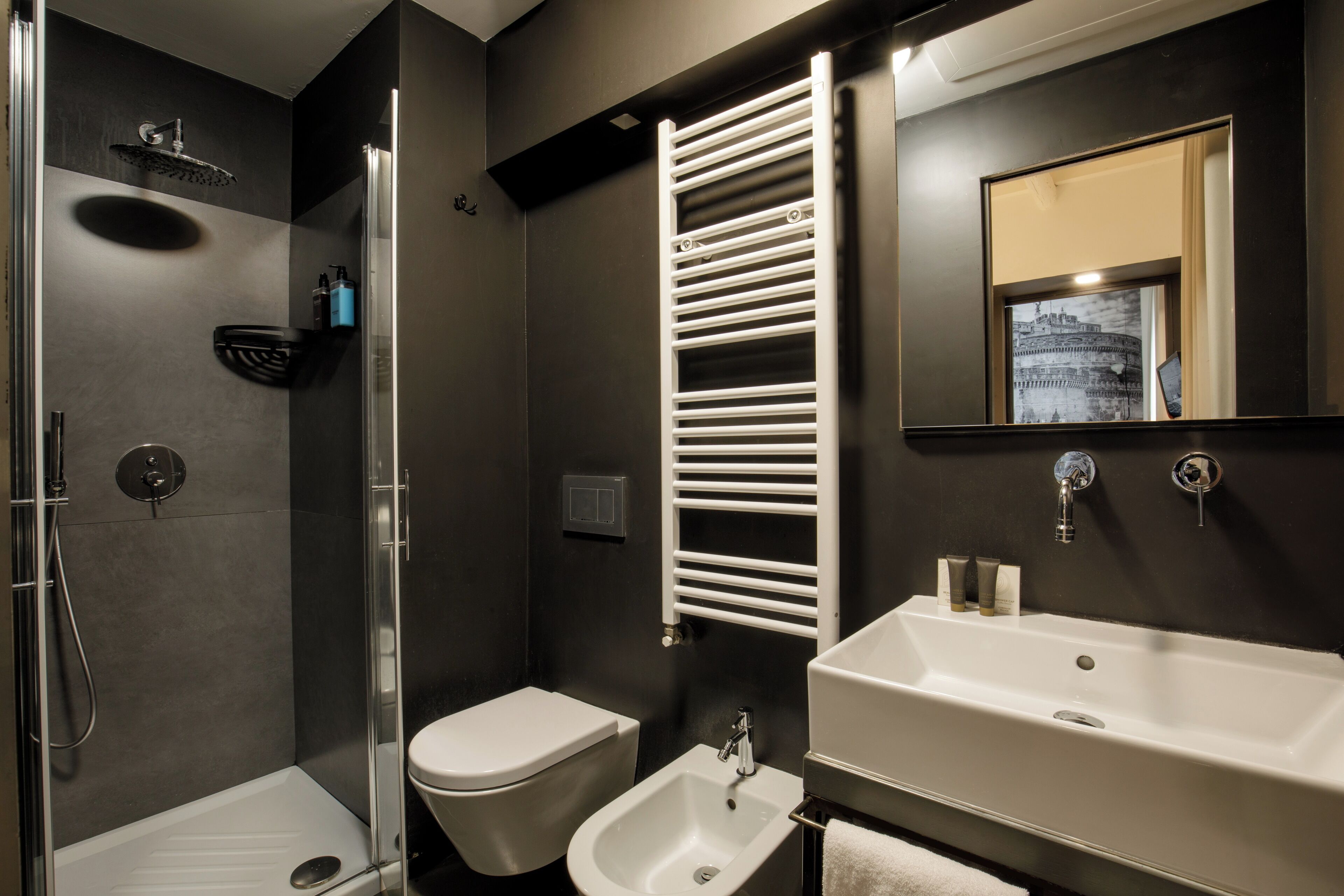 Un baño moderno con ducha envuelta en vidrio, inodoro blanco, bidé y un lavamanos grande y blanco.