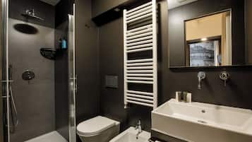 Un baño moderno con ducha envuelta en vidrio, inodoro blanco, bidé y un lavamanos grande y blanco.