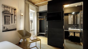 Een moderne hotelkamer met een bed, een stoel, een klein tafeltje, een kapstok, een televisie, een badkamer met spiegel en een raam met gordijnen.