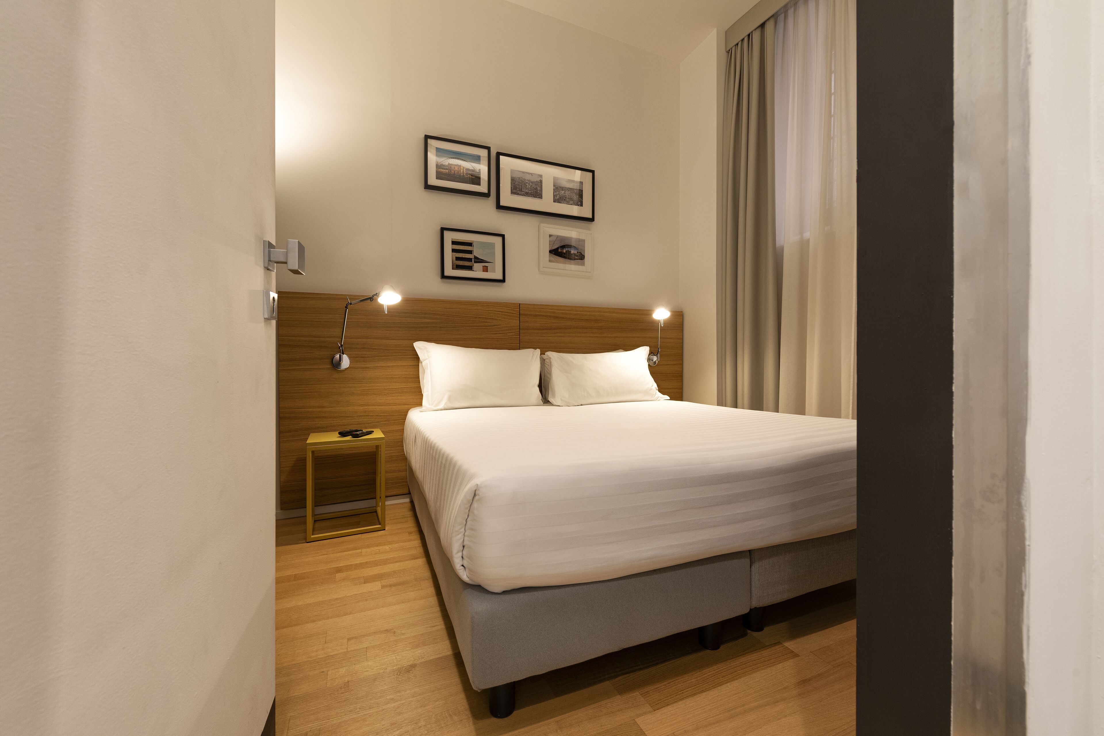 Une chambre d’hôtel moderne avec un grand lit, une tête de lit en bois, des lampes de chevet et des tableaux encadrés accrochés au mur.