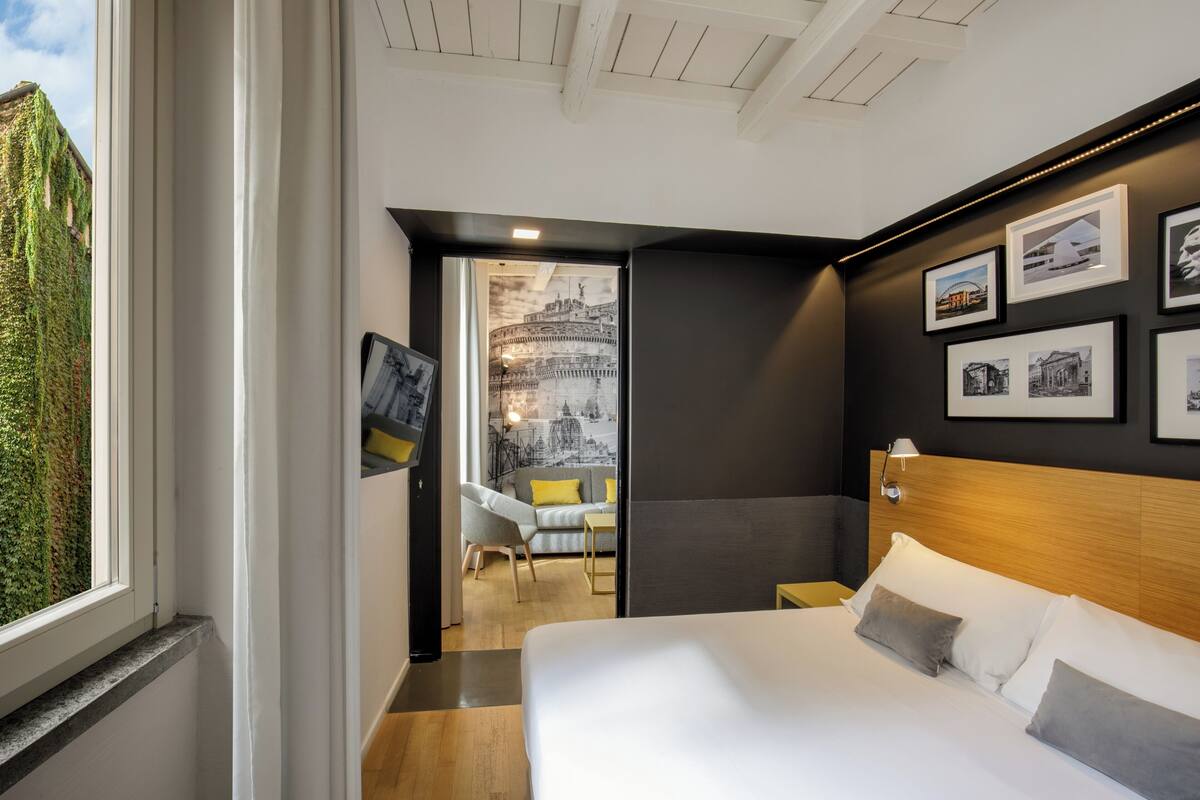 Habitación de hotel moderna con una cama grande, un cabecero de madera y vistas a la ciudad a través de una ventana.