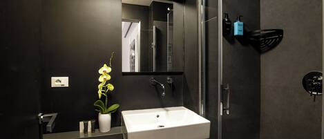 Un baño moderno con un lavamanos blanco, un espejo, una ducha y un perchero para toallas.