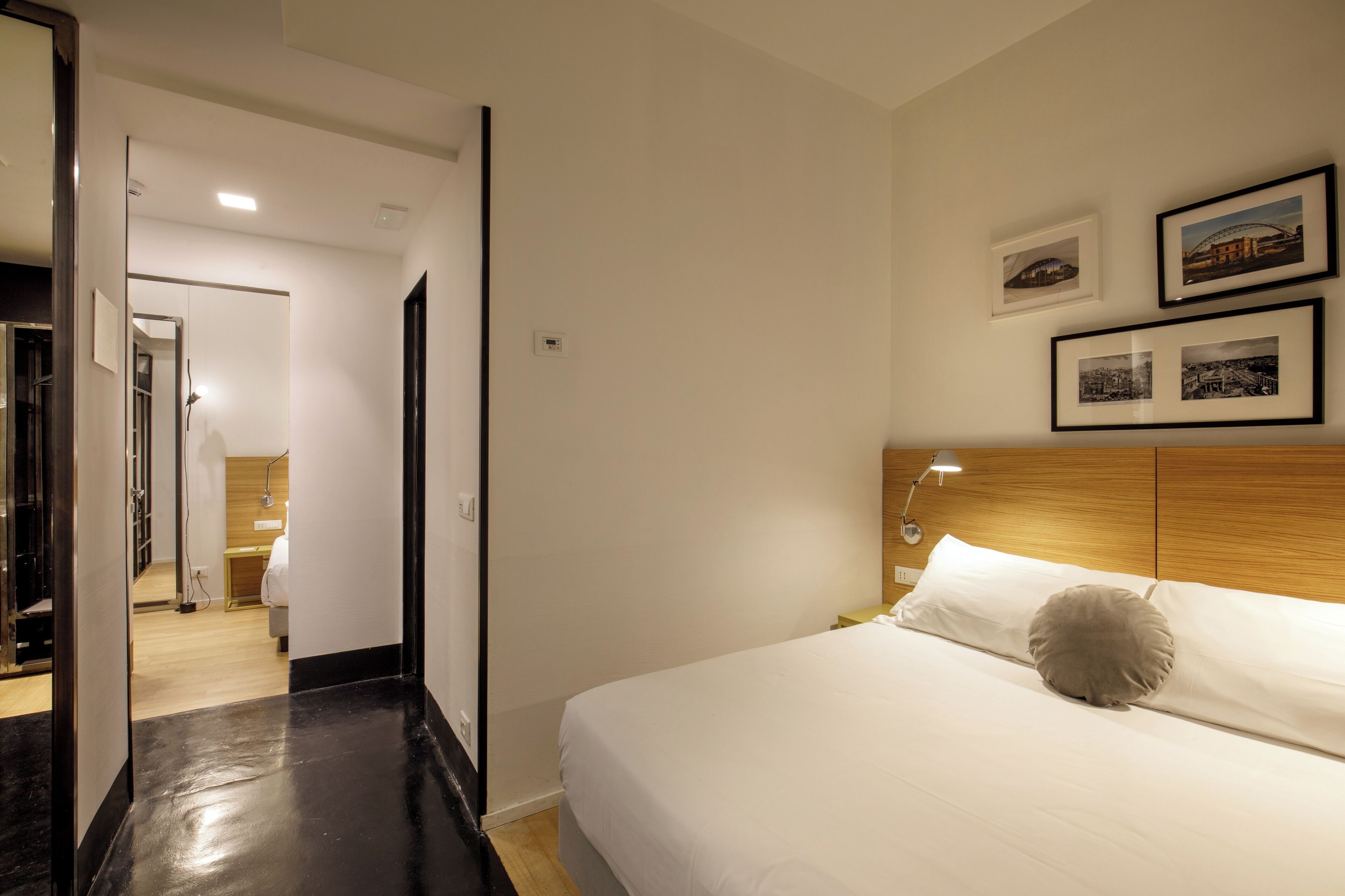 A hotel room with a bed, a nightstand, a lamp, and framed pictures on the wall.
