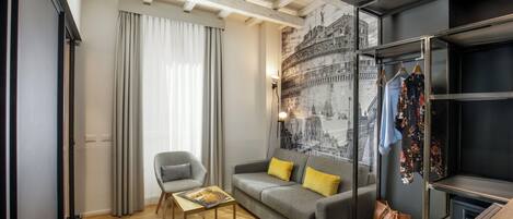 Uma sala de estar moderna com um sofá cinzento, almofadas amarelas, uma mesa de centro de madeira e um cabideiro com roupas penduradas.
