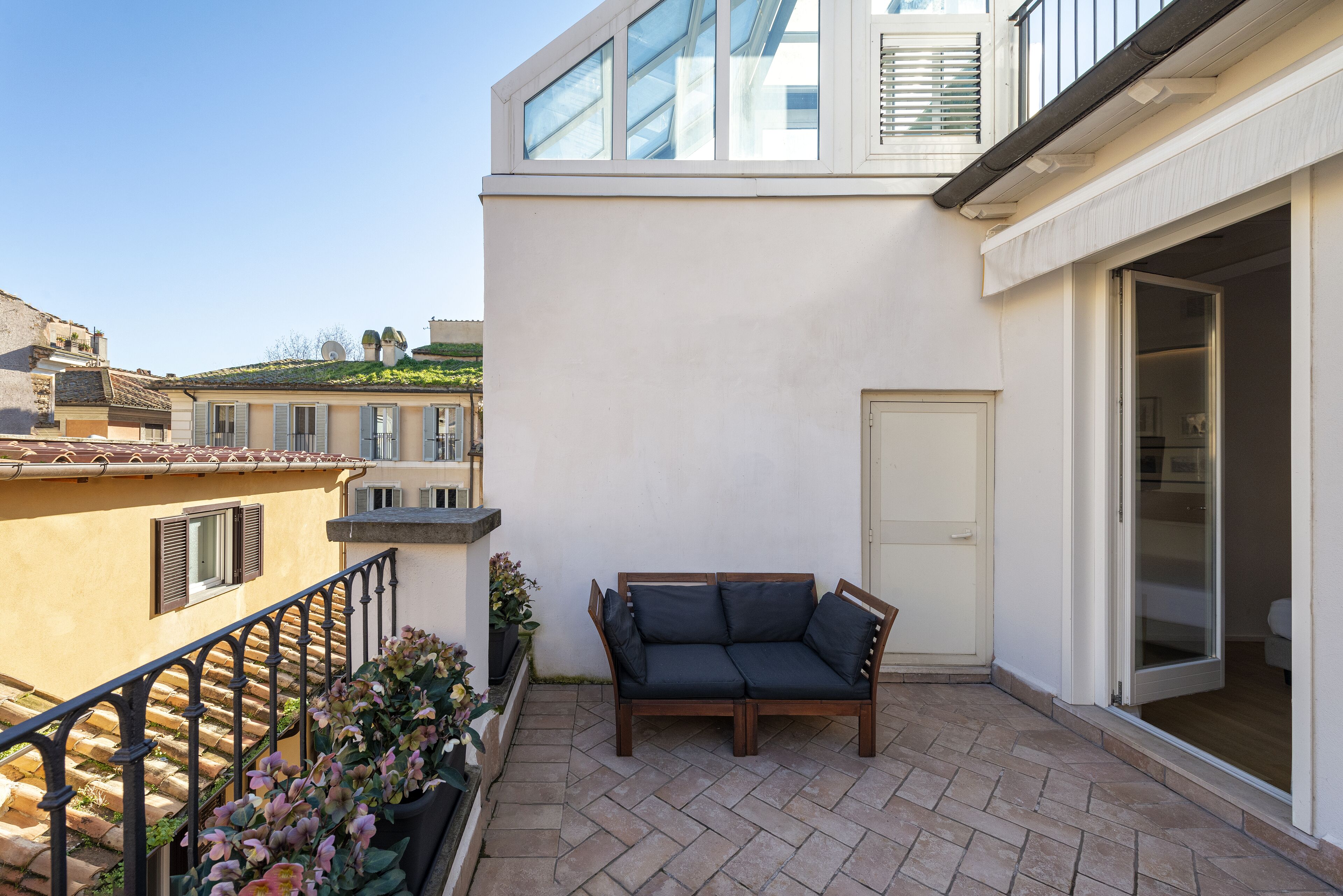 A balcony with a wooden bench, a door, and a view of neighboring buildings.
