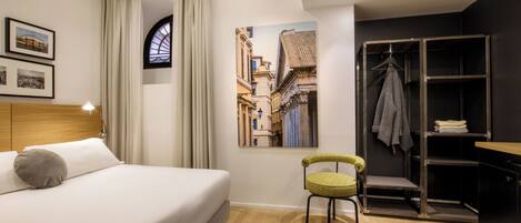 A modern hotel room with a bed, a chair, a wardrobe, and a painting of a street scene.