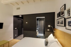 A modern hotel room with a large bed, a bedside table, a shower area, and framed pictures on the wall.
