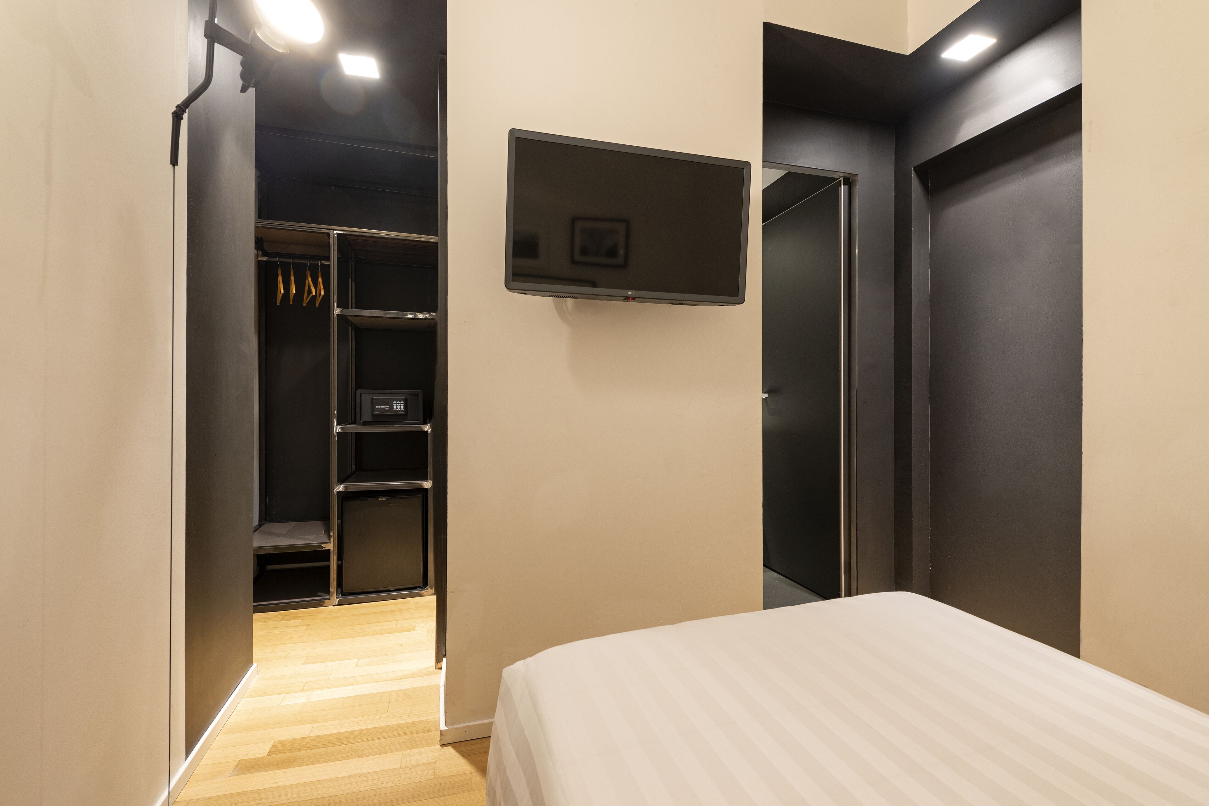 A bedroom with a bed, a TV mounted on the wall, and a closet with shelves.