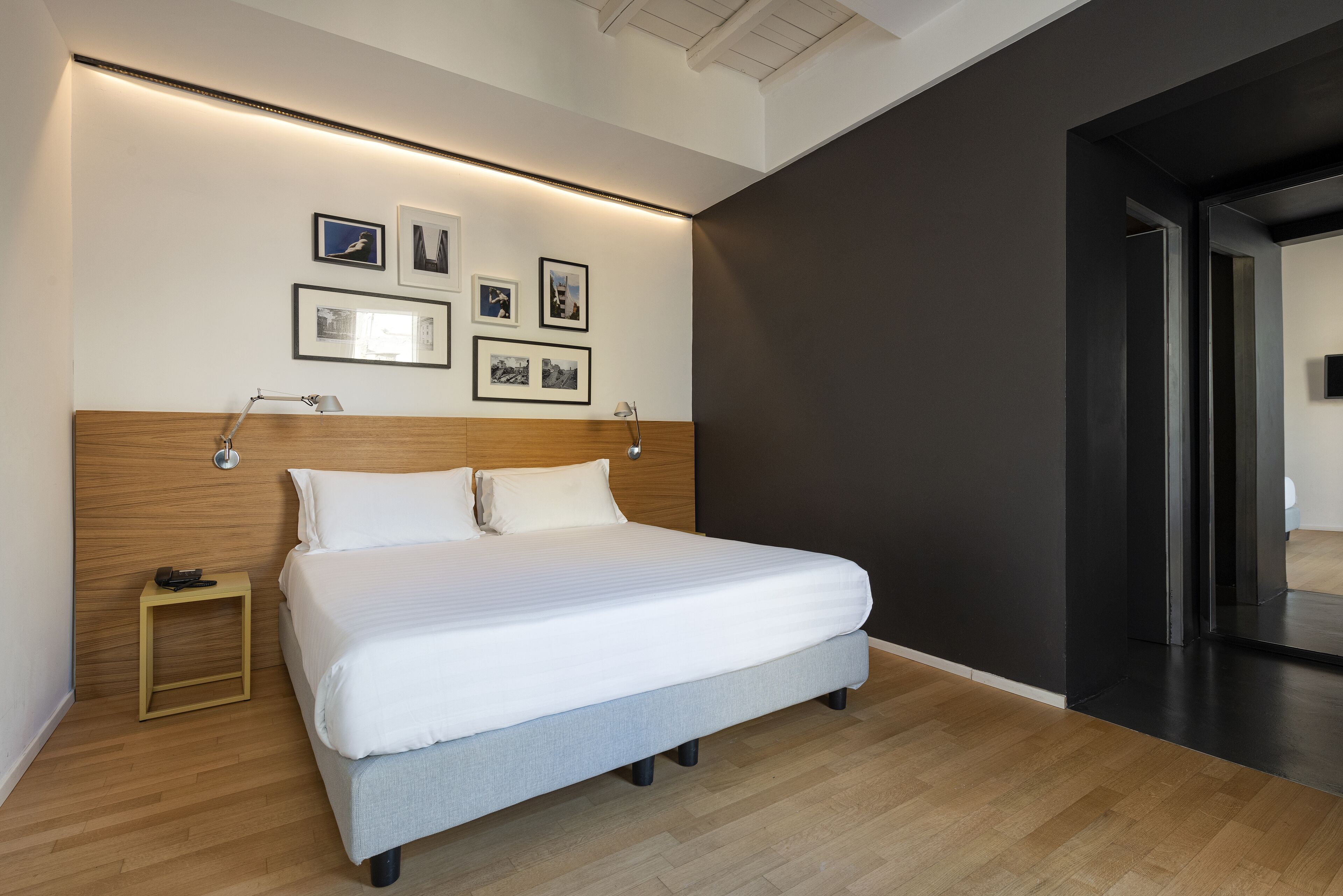 A modern bedroom with a large bed, wooden headboard, bedside tables, and wall-mounted lamps.