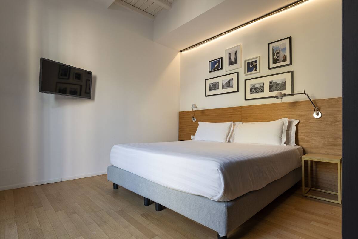 Una habitación de hotel moderna con una cama grande, cabecera de madera y televisor instalado en la pared.