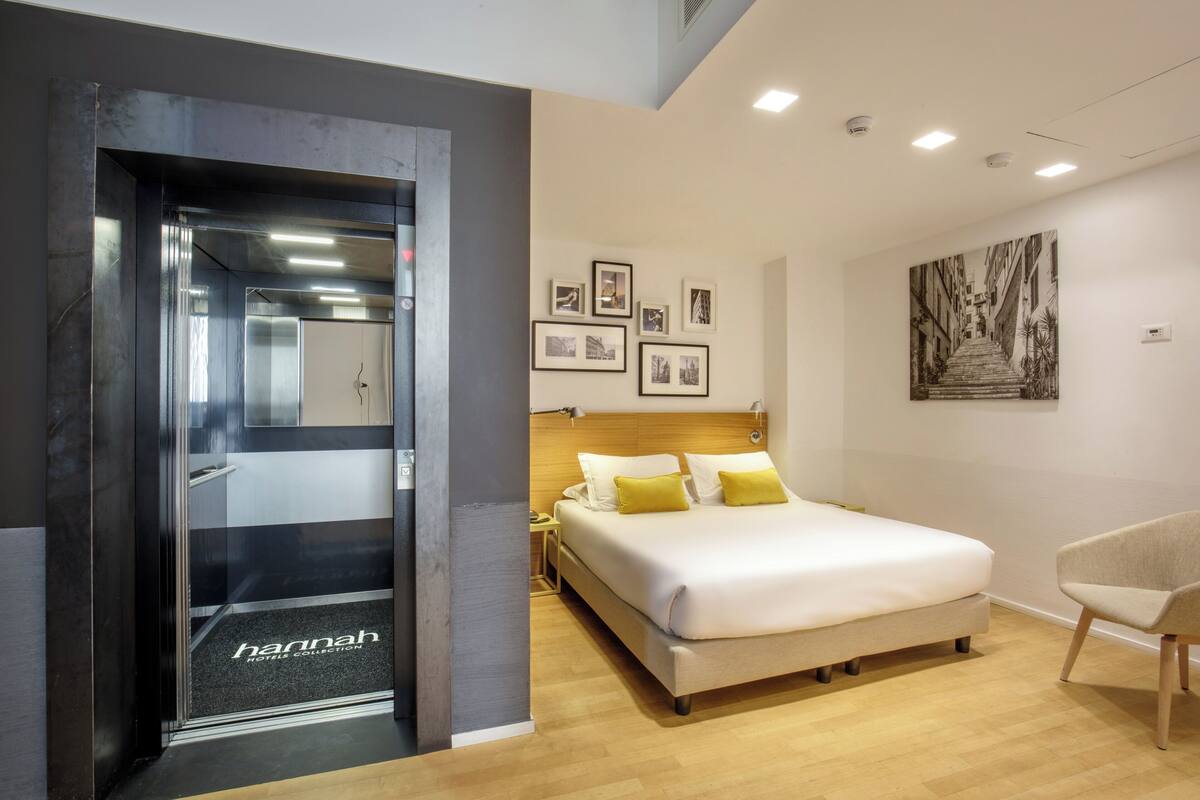 Una habitación de hotel con una cama, una silla, una mesita de noche y una pared decorada con cuadros.