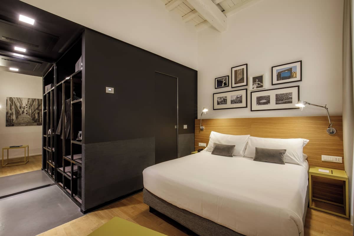 Una habitación de hotel con una cama grande, un armario, una mesita y cuadros en la pared.