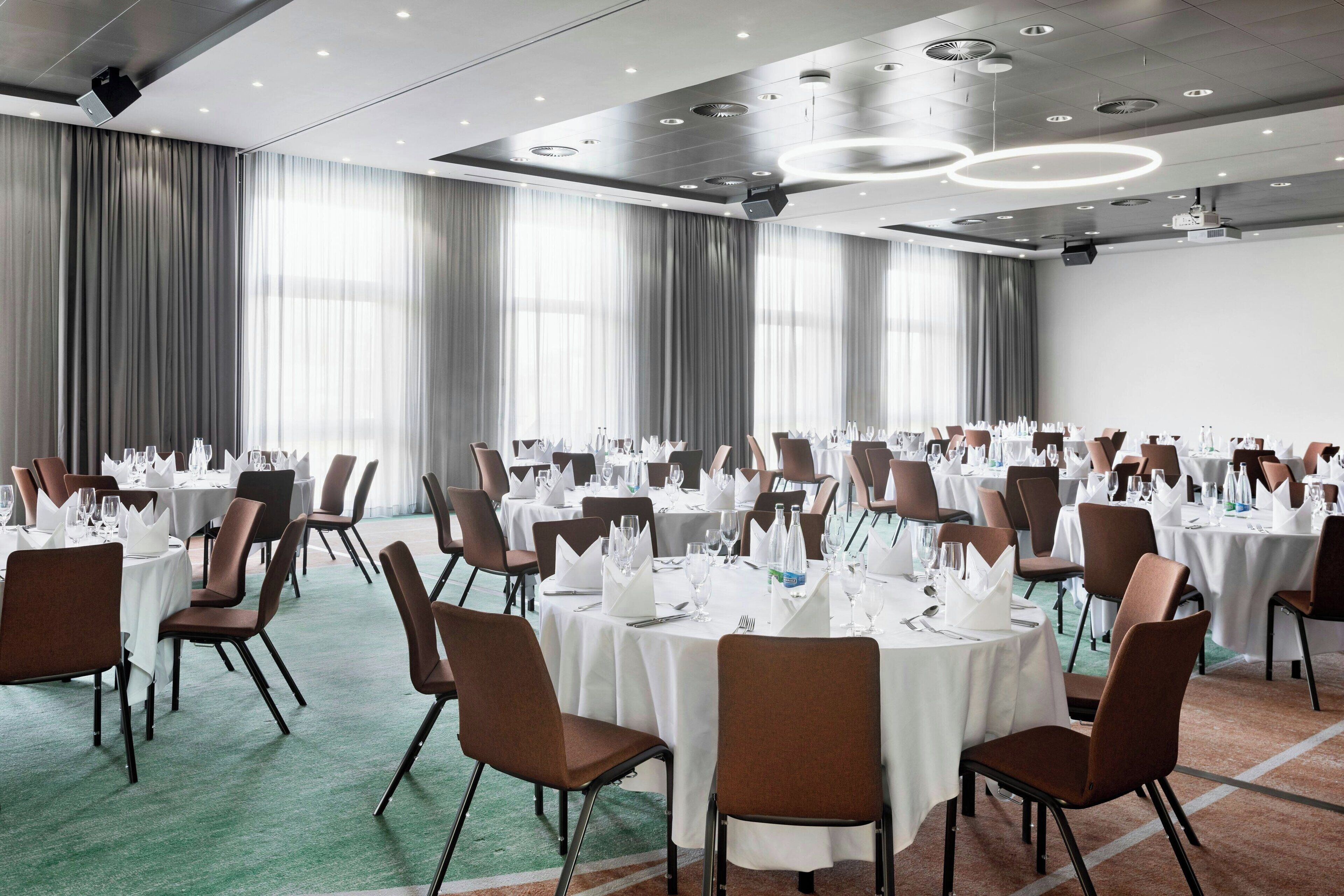A conference room with round tables, chairs, and a projector on the ceiling.