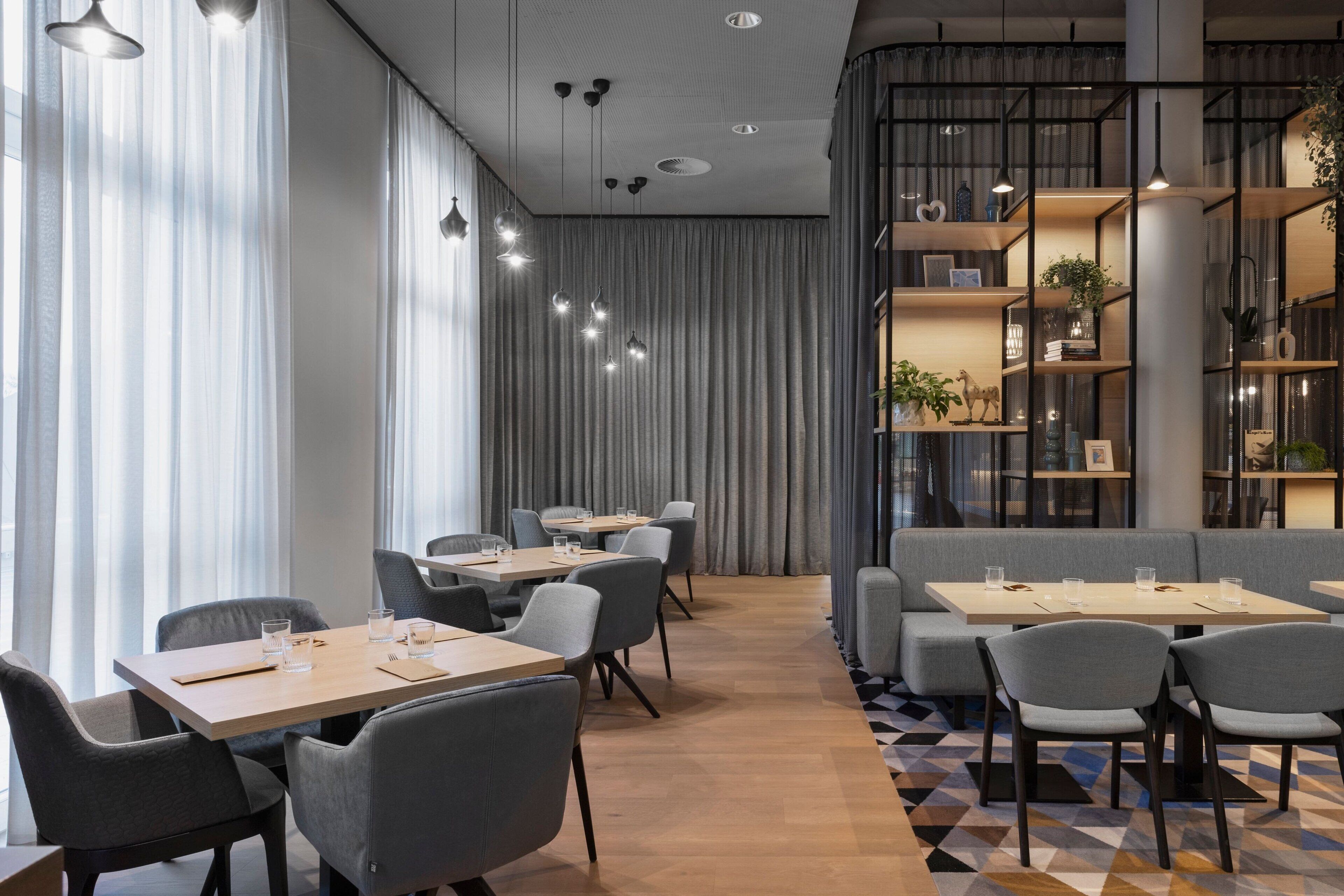 Un comedor moderno con mesas, sillas, suelo estampado y una estantería con objetos decorativos.