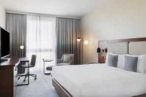 Una habitación de hotel con una cama grande, un escritorio, una silla, un televisor y una lámpara.