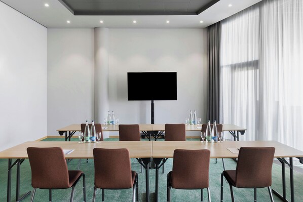 A conference room with a large table, chairs, a flat-screen TV, and a window with curtains.