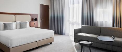 A modern hotel room with a large bed, a sofa, a small table, and a door.