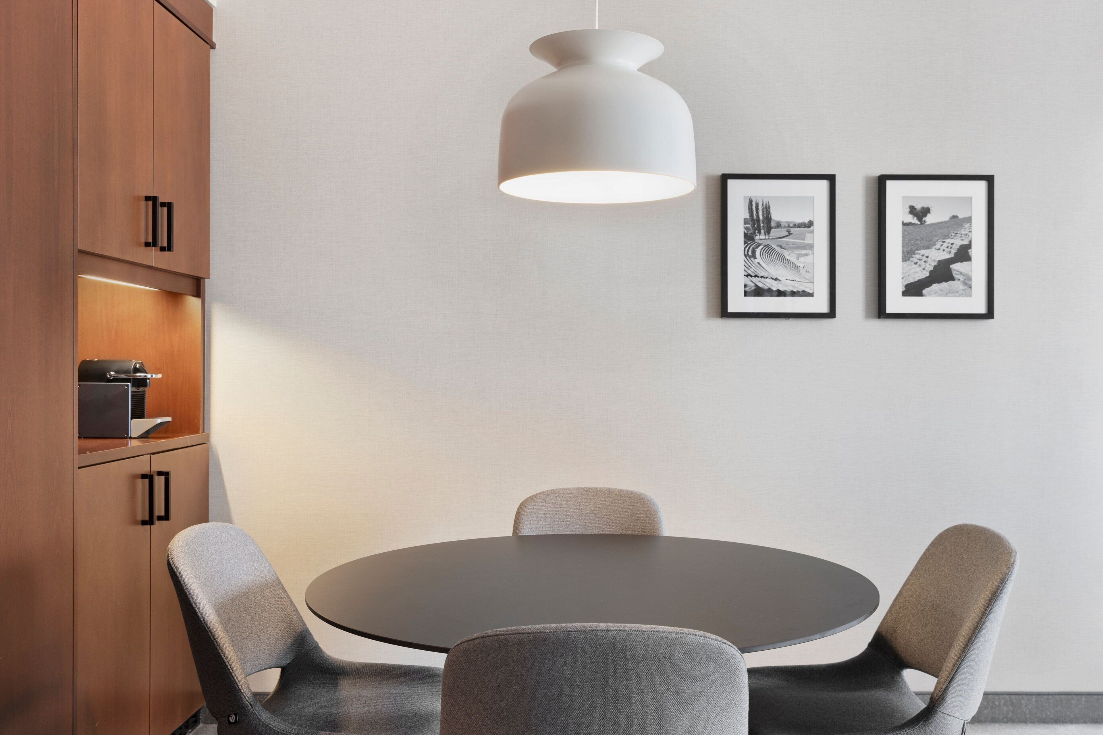 A modern dining area with a round table, four chairs, a pendant light, and two framed pictures on the wall.