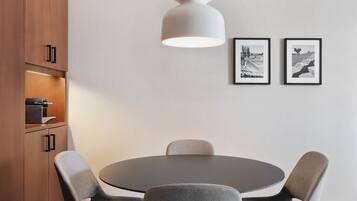 A modern dining area with a round table, four chairs, a pendant light, and two framed pictures on the wall.