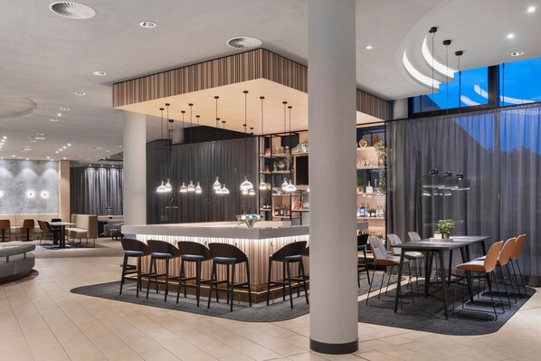 A modern hotel lobby with a bar area, seating arrangements, and a large window providing a view. - Courtyard by Marriott Basel (Pratteln)