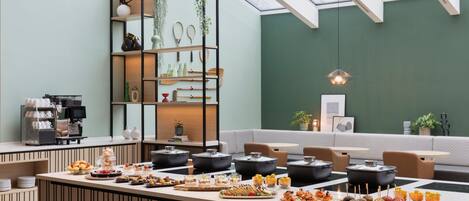 A modern dining area with a central island featuring a variety of food items, surrounded by seating and a green wall with a skylight.