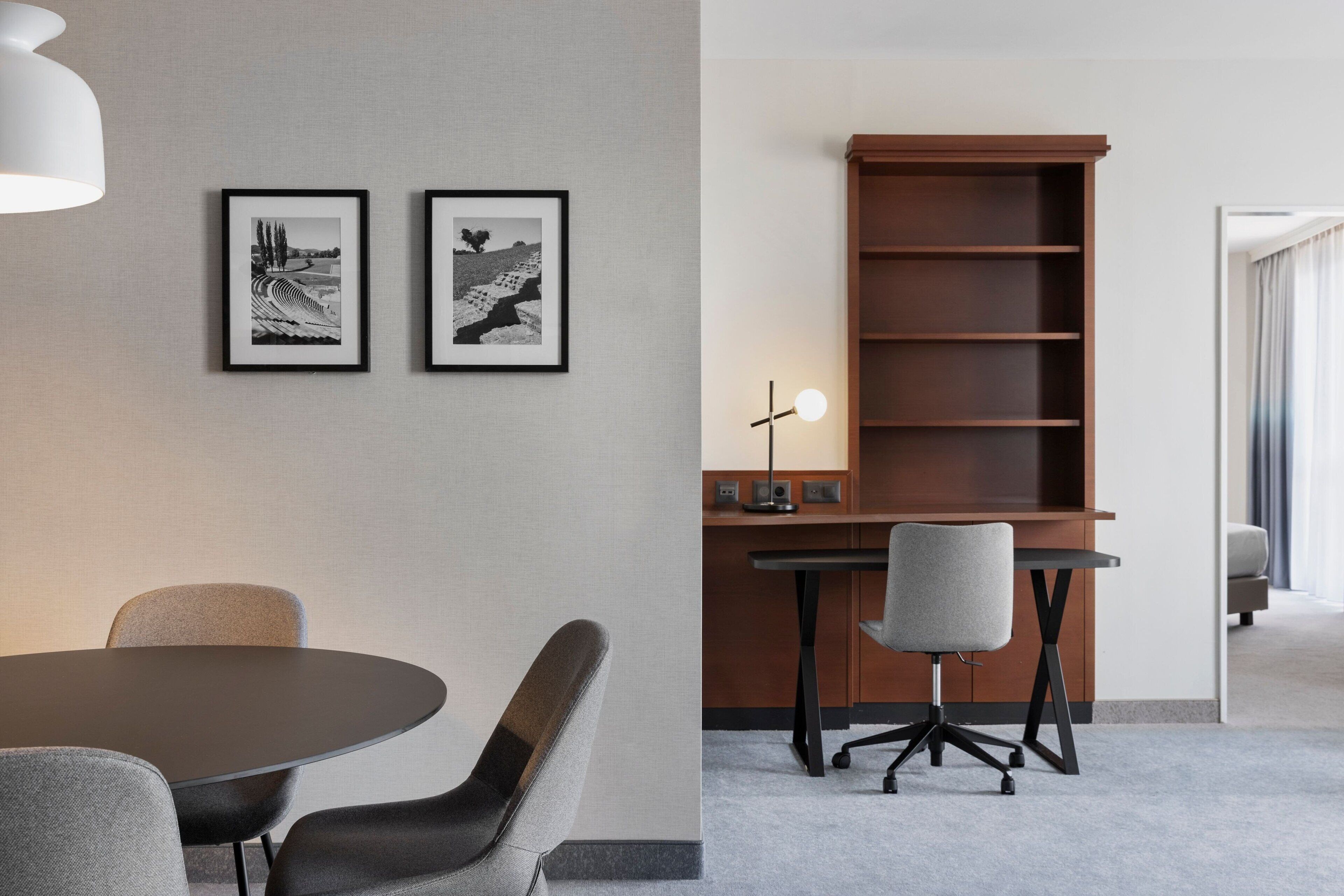 Une salle de conférence moderne avec une table ronde, deux photographies en noir et blanc encadrées accrochées au mur, une bibliothèque en bois et un bureau avec une lampe.