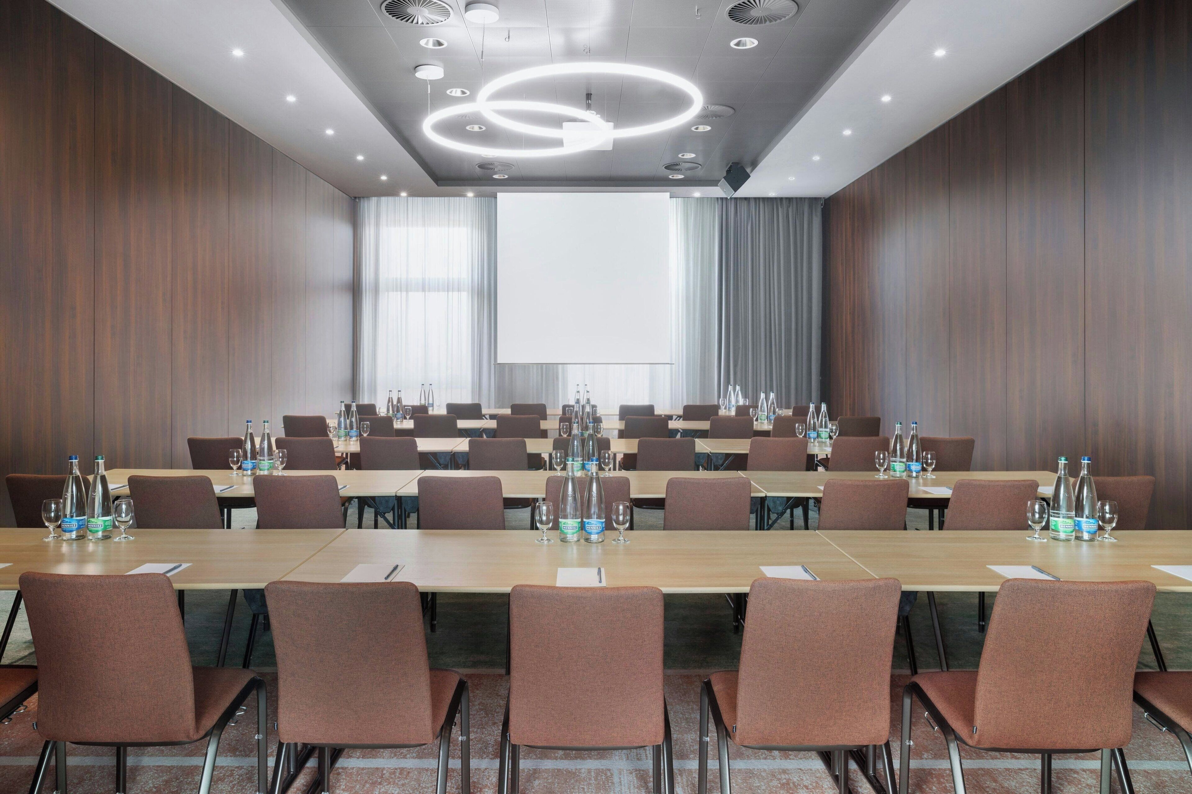 A conference room with a long table, chairs, and a projector screen.
