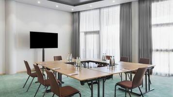 A conference room with a large table, chairs, a flat-screen TV, and curtains.