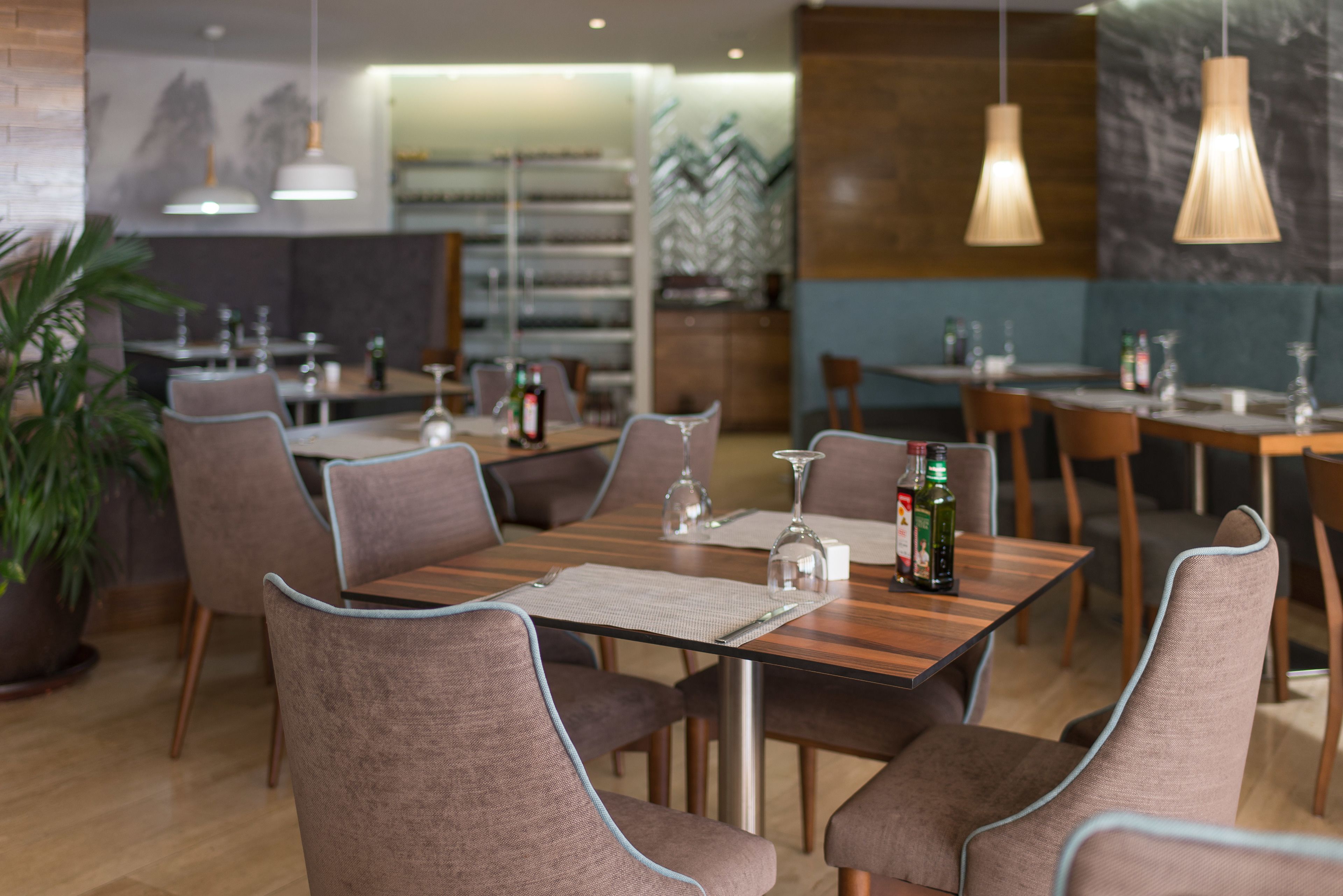 Un interior de restaurante moderno con mesas de madera, sillas tapizadas y lámparas colgantes.