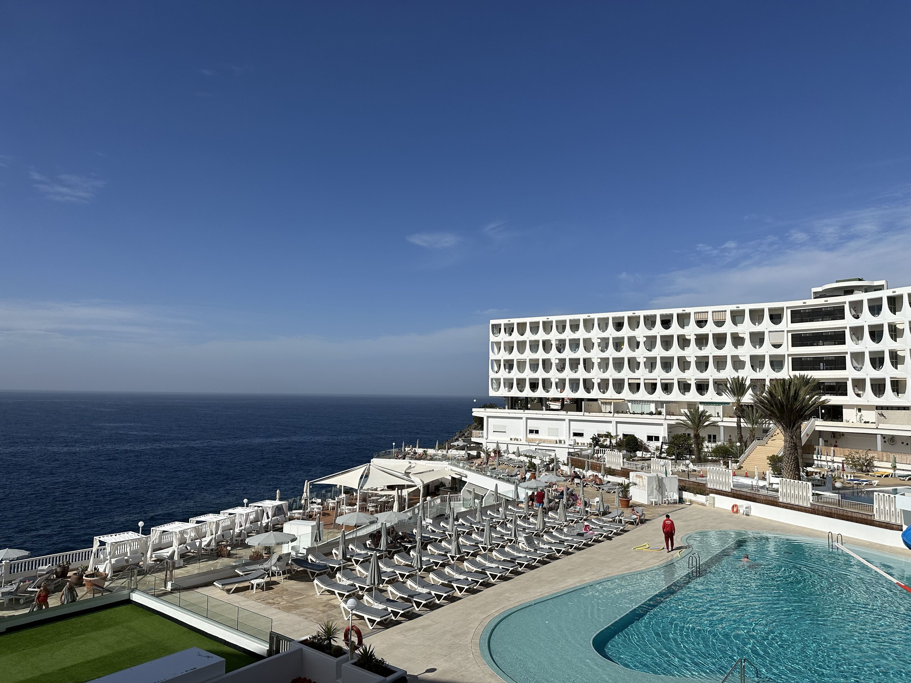 A hotel with a pool, sun loungers, and a view of the ocean.