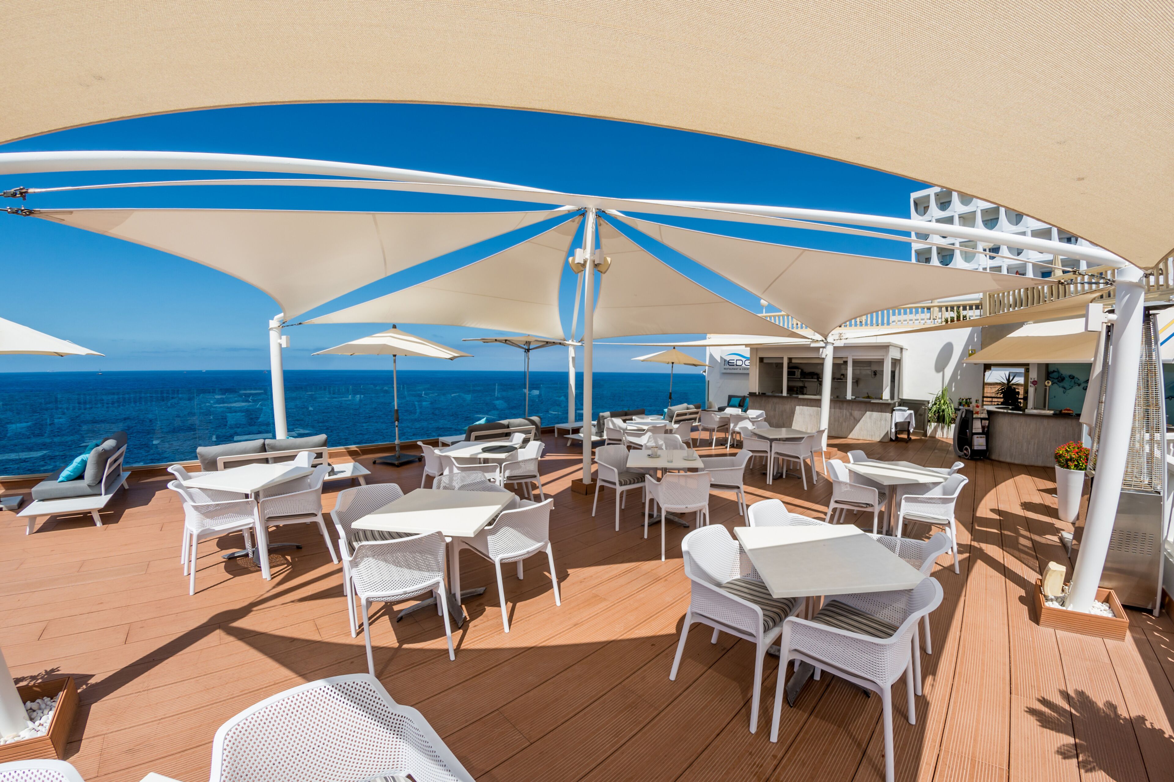 A deck with white tables and chairs, umbrellas, and a view of the ocean.