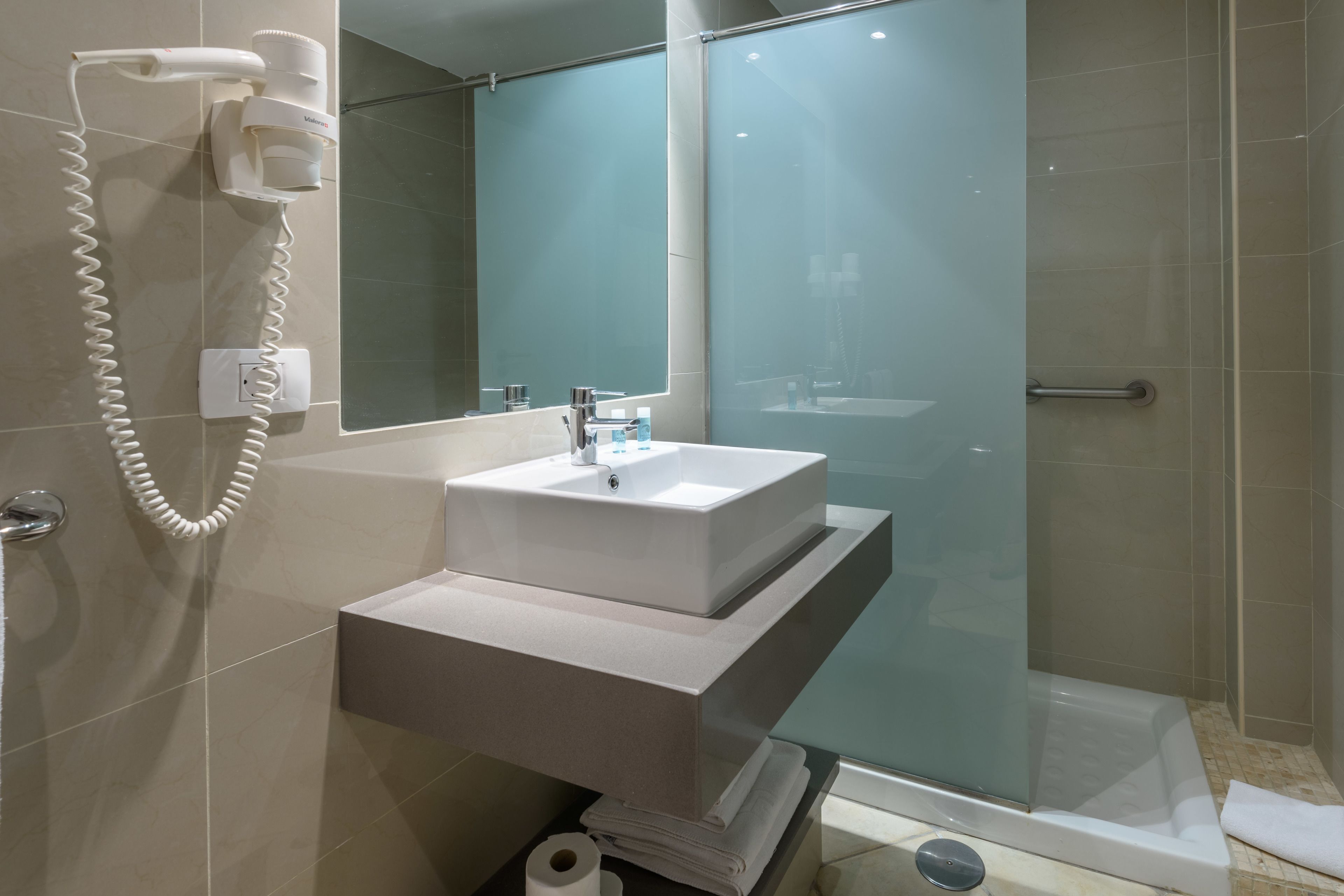 A modern bathroom with a white sink, a hairdryer, and a glass shower enclosure.