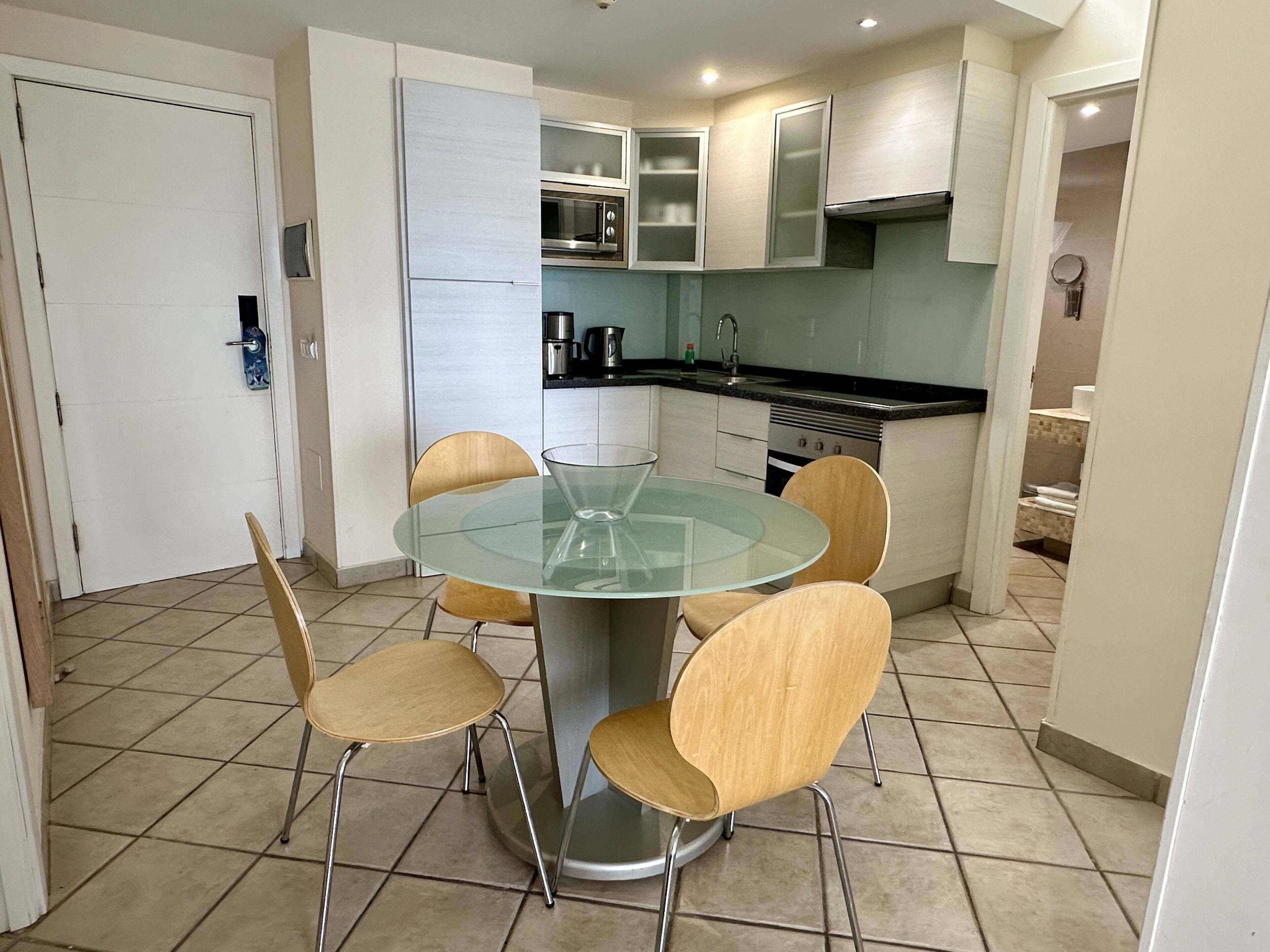 A compact kitchen with a glass-top dining table and four chairs, a microwave, and a stove.