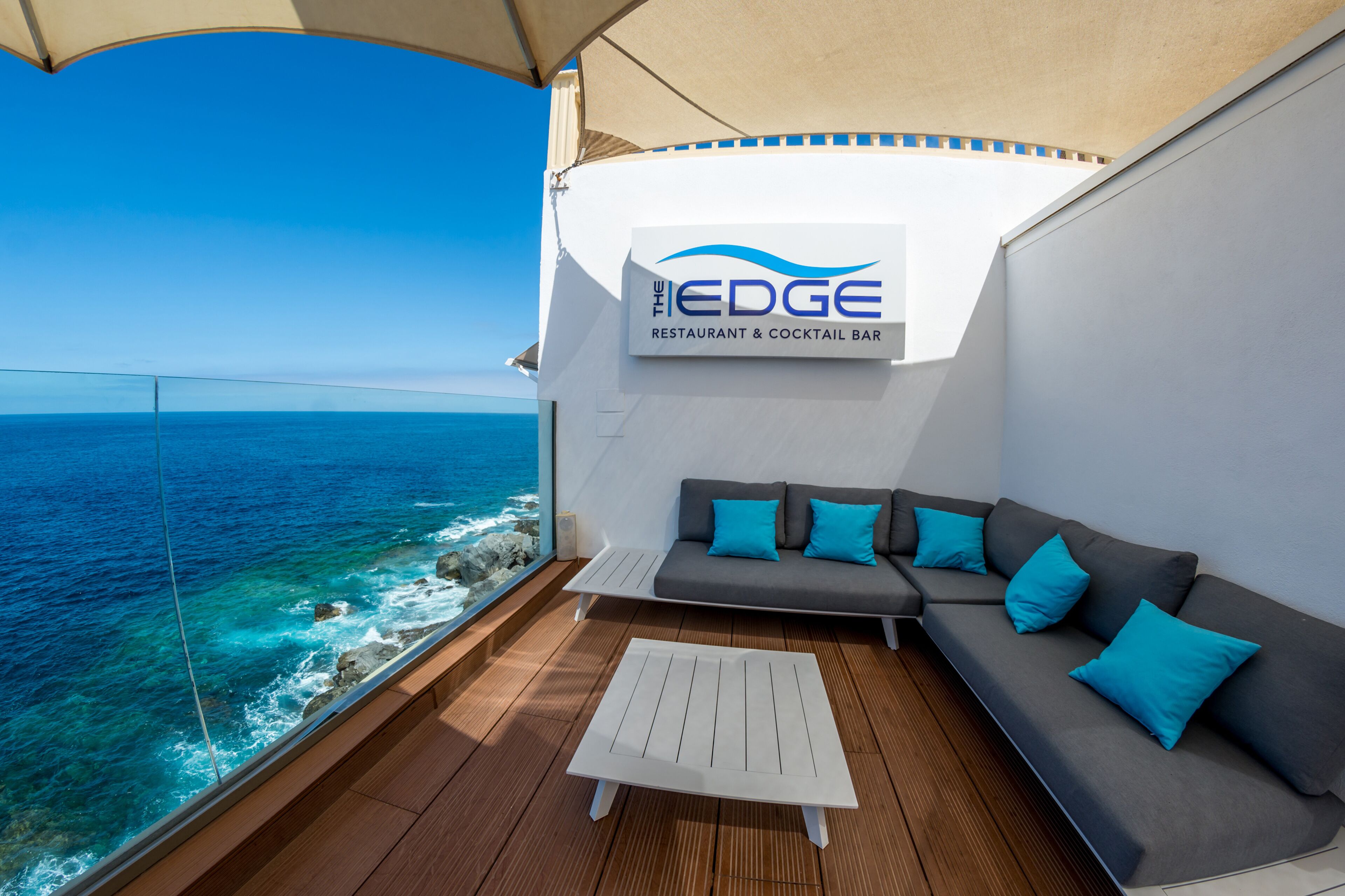 Un balcon avec un canapé et une table basse, donnant sur l’océan. On peut voir une enseigne indiquant « The EDGE Restaurant & Cocktail Bar ».