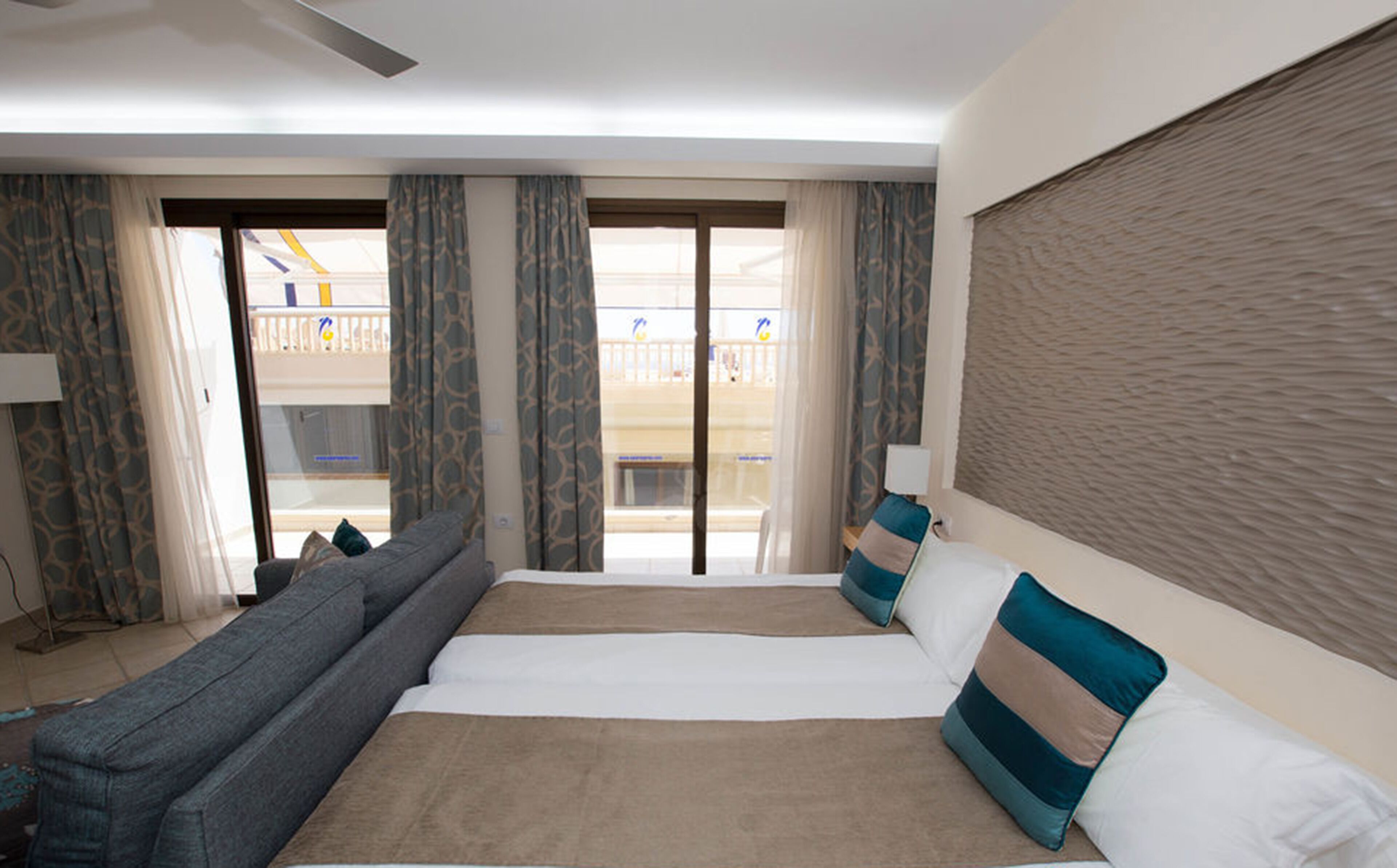 A hotel room with a large bed, a sofa, a balcony with a view, and a window with curtains.