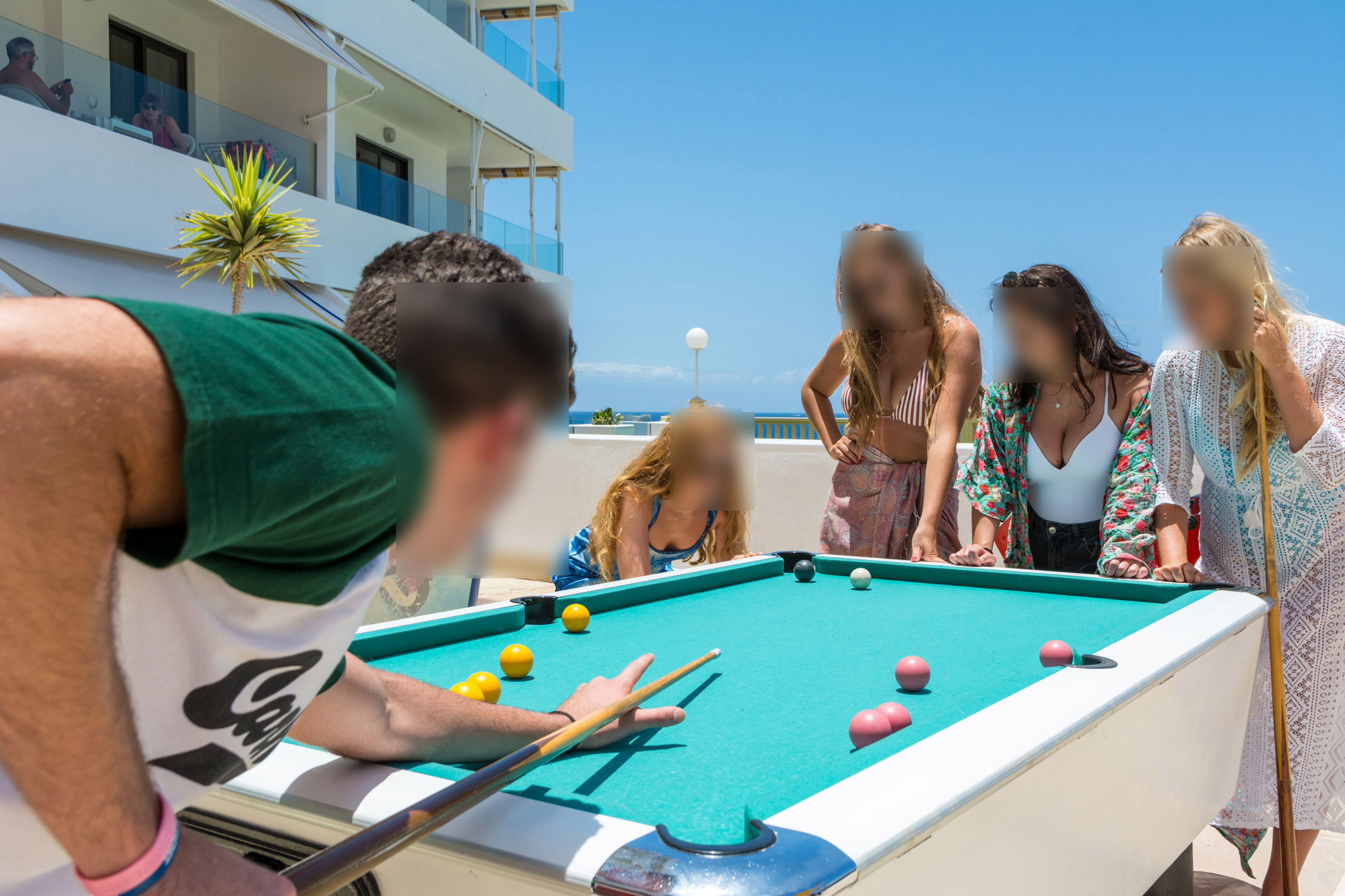 Una mesa de billar con jugadores, cielo despejado y un edificio con balcones.