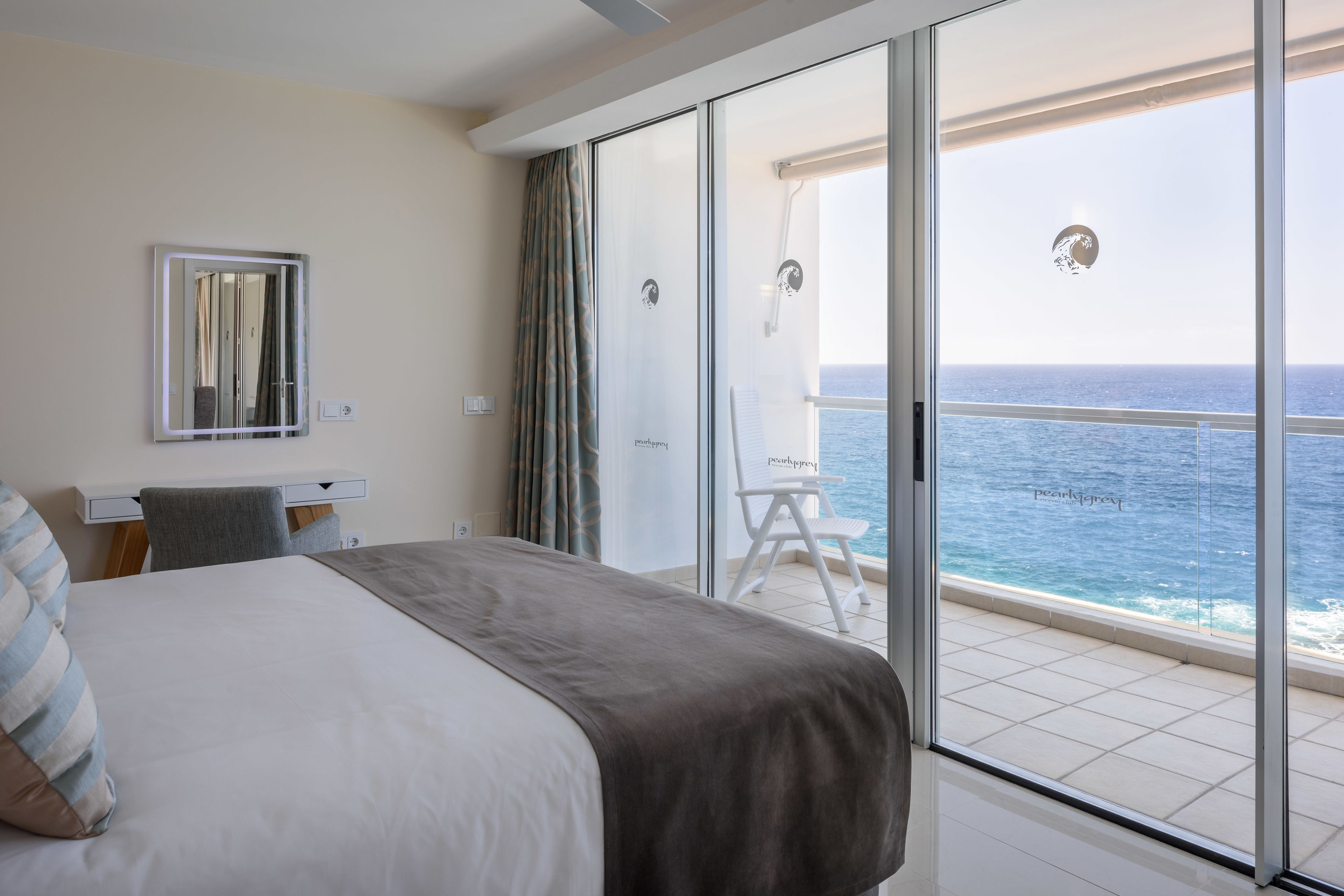 Een hotelkamer met een bed, een bureau, een stoel en een balkon met uitzicht op zee.