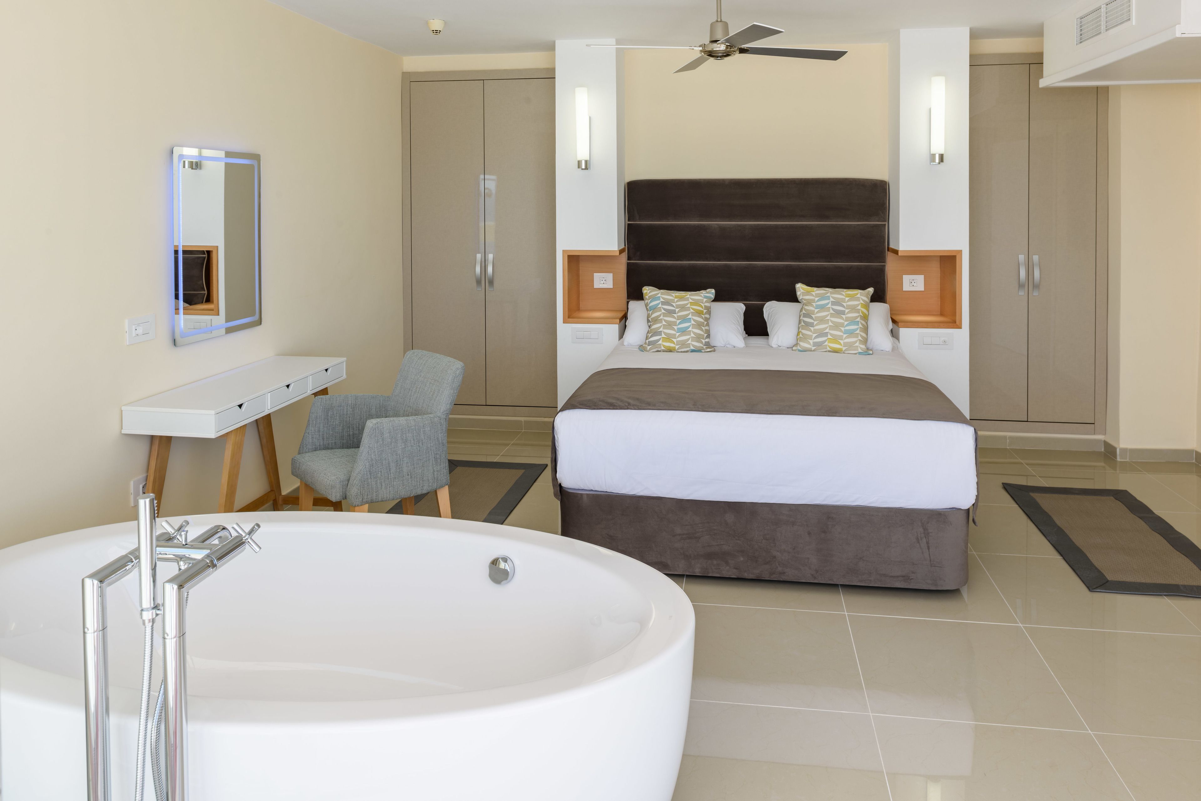Habitación de hotel moderna con una cama grande, zona de estar separada, bañera y ventilador de techo.