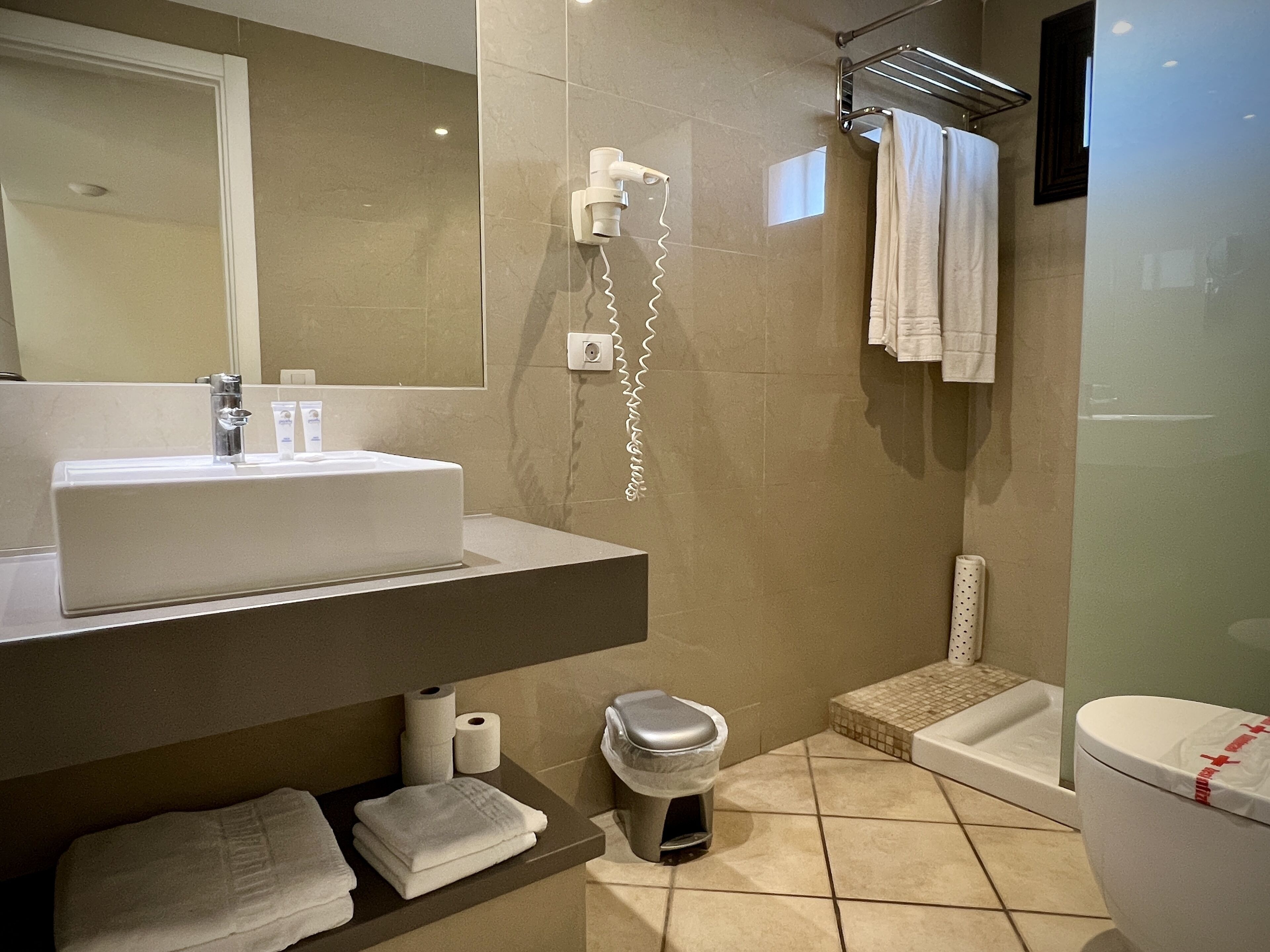 Une salle de bain moderne comprenant un lavabo, un miroir, un porte-serviettes, des toilettes et un espace douche.