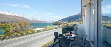A balcony with a table, chairs, and a scenic view of a lake and mountains.