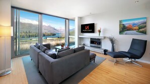 Una sala de estar moderna con un sofá grande, un televisor de pantalla plana montado en la pared, una chimenea y una vista panorámica a través de amplios ventanales.