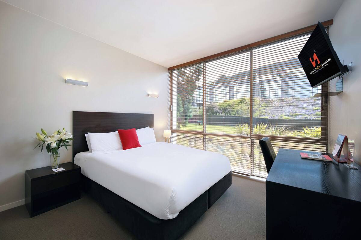 Una habitación de hotel con una cama grande, un escritorio y una ventana con persianas.