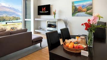 A modern living room with a fireplace, a dining table with a fruit bowl, and a scenic mountain view through the window.