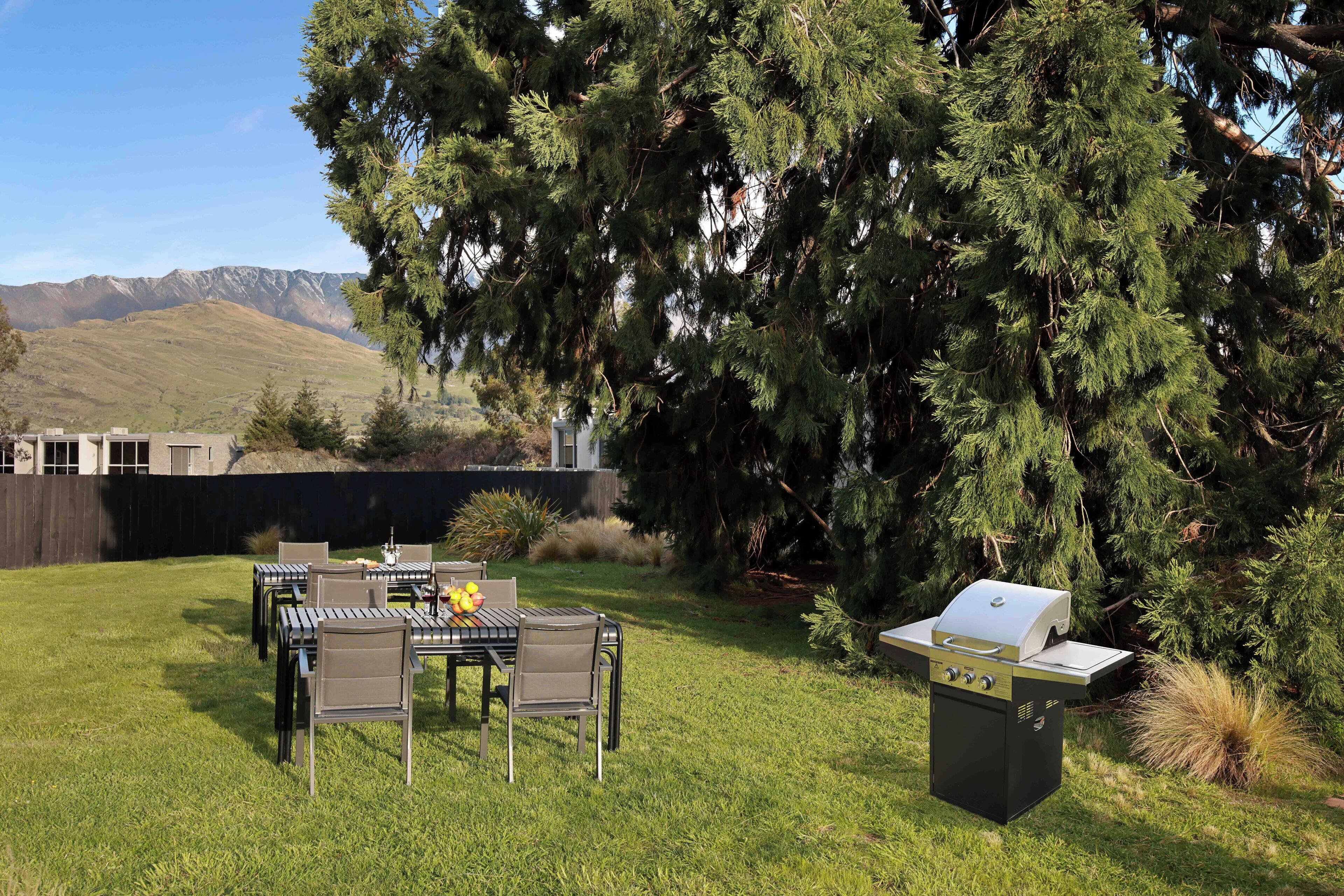 Un patio trasero con una mesa y sillas de comedor, una parrilla y un árbol grande.