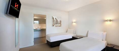 A hotel room with two beds, a TV, a painting, and a bathroom visible through an open door.